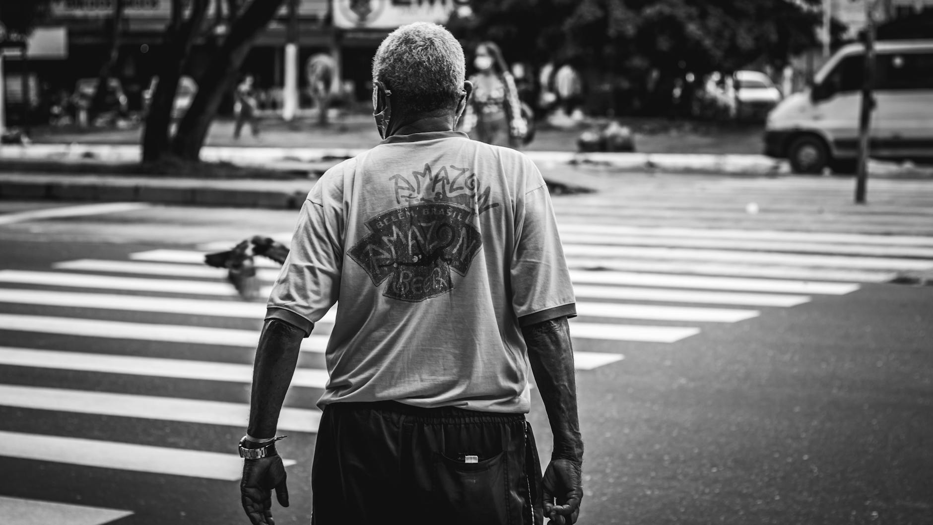 Czarno-białe zdjęcie mężczyzny przechodzącego po pasach w mieście