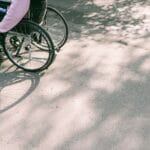 Osoba na wózku inwalidzkim na słonecznej drodze wśród cieni drzew